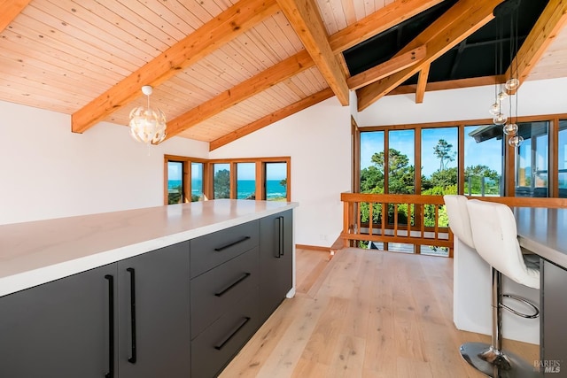 kitchen featuring hanging light fixtures, lofted ceiling with beams, light countertops, light wood-type flooring, and dark cabinetry