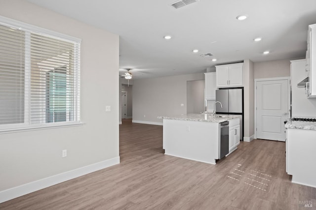 kitchen featuring light stone counters, white cabinets, appliances with stainless steel finishes, and an island with sink