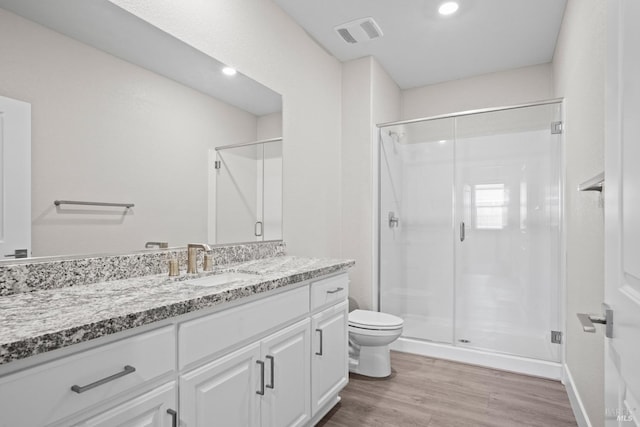 bathroom with hardwood / wood-style floors, toilet, a shower with shower door, and vanity