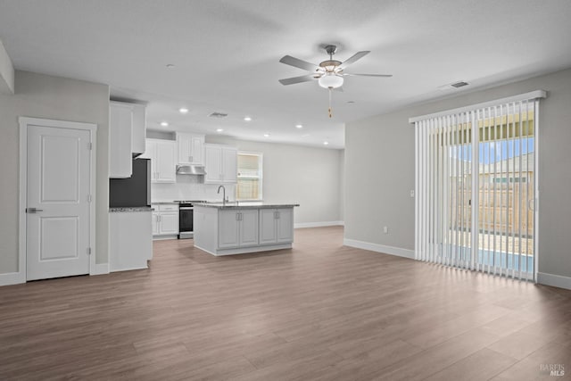 kitchen featuring refrigerator, stainless steel stove, a kitchen island with sink, white cabinets, and backsplash