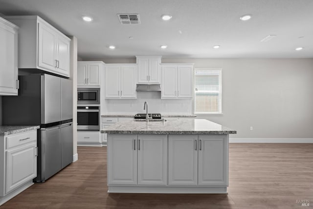 kitchen with light stone countertops, hardwood / wood-style floors, white cabinets, stainless steel appliances, and tasteful backsplash