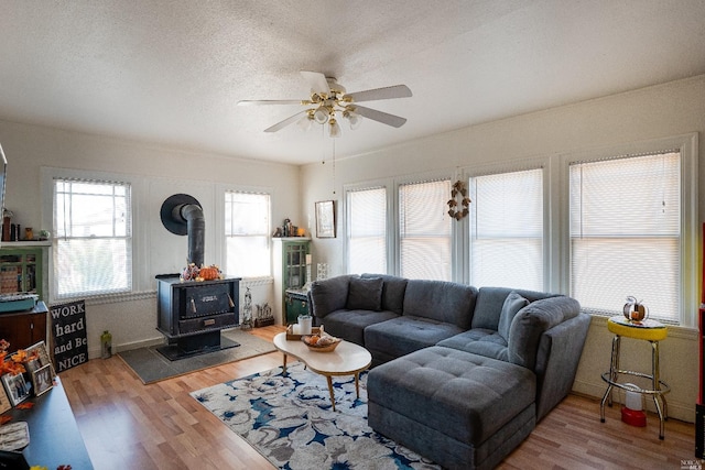 living room featuring a textured ceiling, ceiling fan, a wood stove, and light hardwood / wood-style flooring