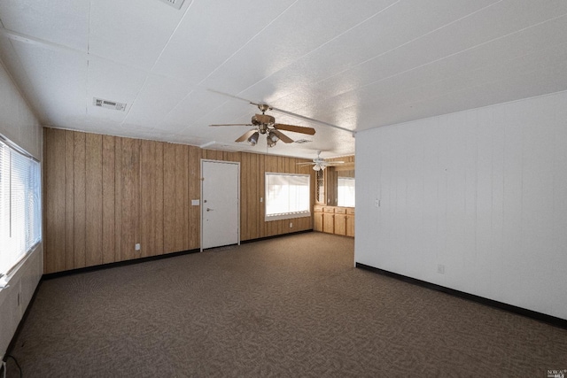 unfurnished room featuring dark colored carpet, wood walls, and ceiling fan