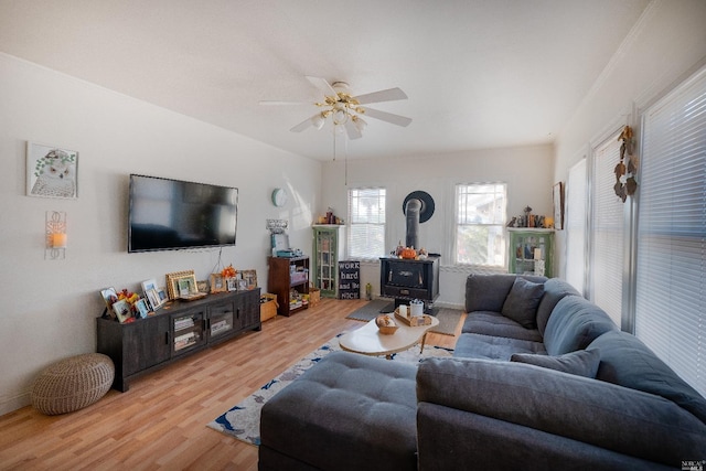 living room with light hardwood / wood-style floors, ceiling fan, and a wood stove