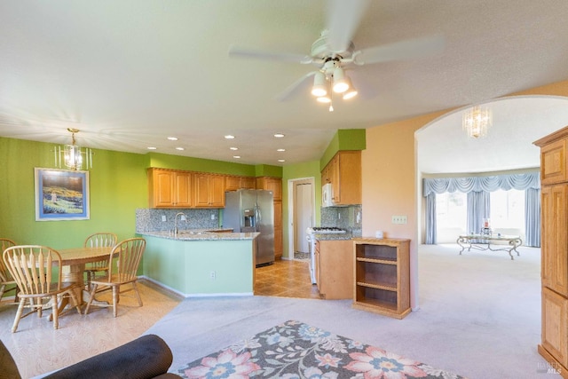 kitchen featuring ceiling fan with notable chandelier, stainless steel fridge, decorative backsplash, and light carpet