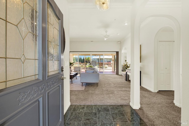 entryway featuring crown molding, ceiling fan, arched walkways, dark carpet, and baseboards