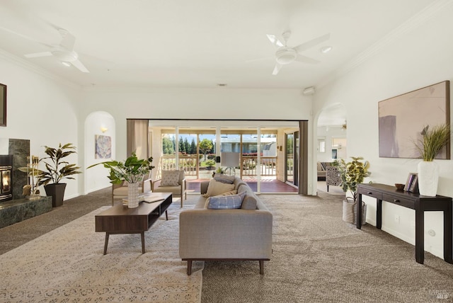 carpeted living area with crown molding, arched walkways, ceiling fan, and a premium fireplace
