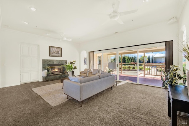 carpeted living room featuring crown molding, ceiling fan, a fireplace, arched walkways, and recessed lighting
