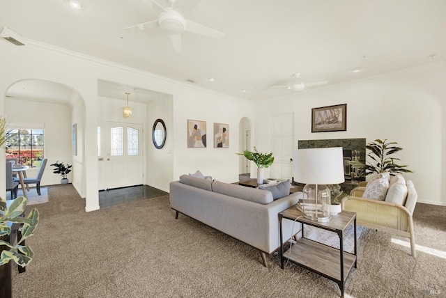 living area with arched walkways, a ceiling fan, ornamental molding, and carpet