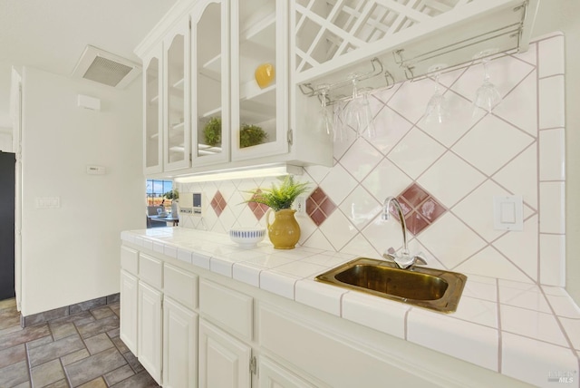 kitchen with a sink, white cabinetry, decorative backsplash, visible vents, and glass insert cabinets
