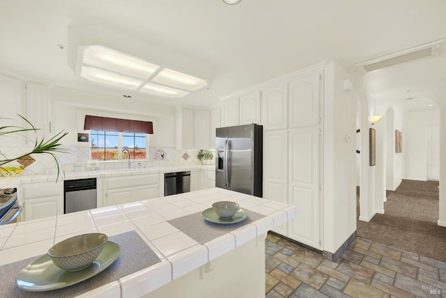 kitchen with tile countertops, stainless steel fridge, a sink, and dishwashing machine