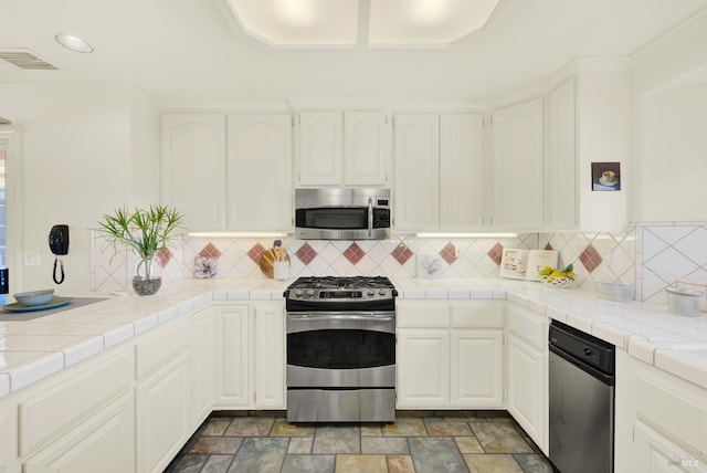 kitchen featuring decorative backsplash, white cabinetry, tile counters, and stainless steel appliances