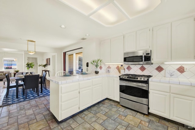 kitchen with kitchen peninsula, stainless steel appliances, tile counters, and a wealth of natural light