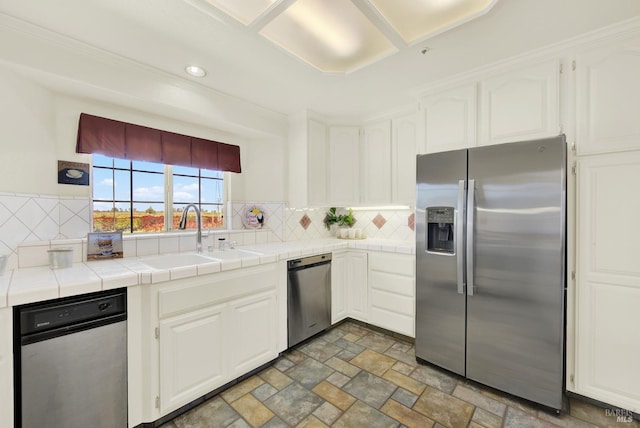 kitchen with appliances with stainless steel finishes, tasteful backsplash, sink, white cabinetry, and tile counters