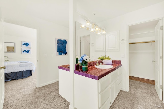 bathroom featuring vanity, baseboards, carpet, and a walk in closet