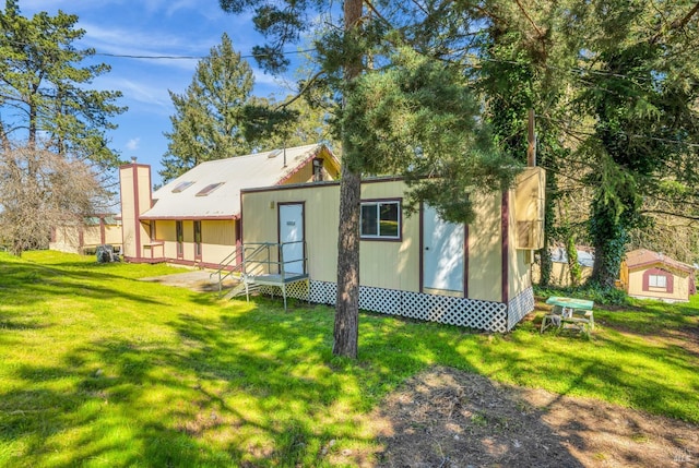 rear view of property featuring a lawn, a chimney, and entry steps
