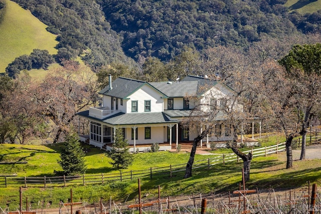 farmhouse-style home with a rural view, a front lawn, and covered porch