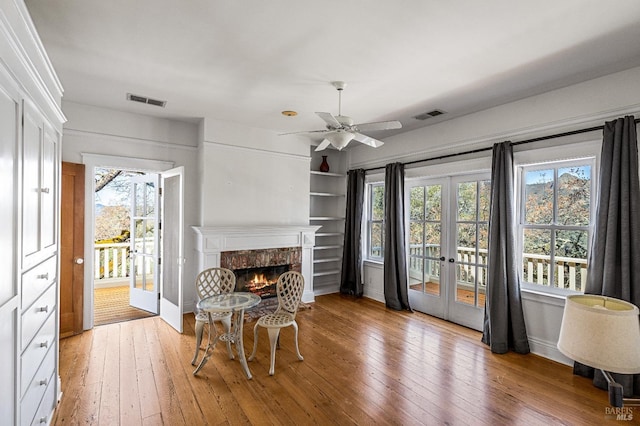 interior space featuring ceiling fan, light hardwood / wood-style flooring, french doors, and a fireplace