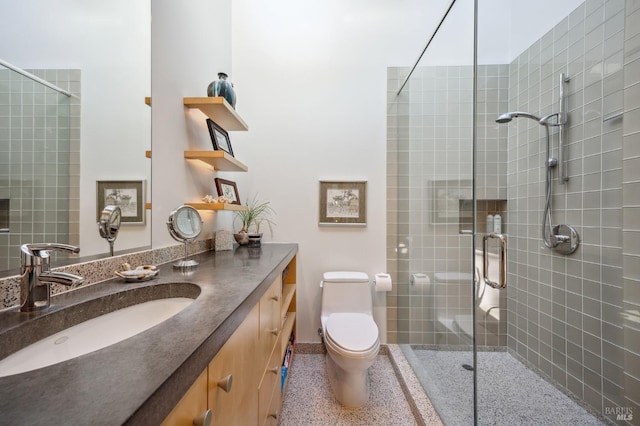 bathroom with toilet, vanity, speckled floor, baseboards, and a tile shower