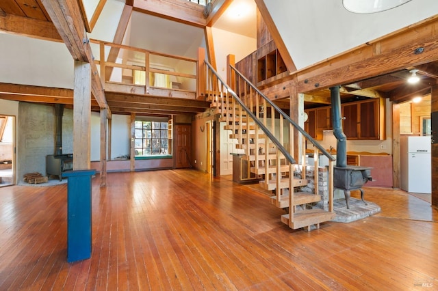 unfurnished living room with a wood stove, hardwood / wood-style floors, high vaulted ceiling, and beamed ceiling