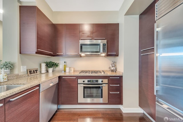 kitchen with dark hardwood / wood-style flooring, dark brown cabinets, light stone countertops, and appliances with stainless steel finishes