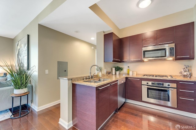 kitchen with appliances with stainless steel finishes, sink, light stone counters, kitchen peninsula, and dark wood-type flooring