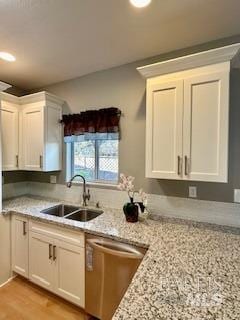 kitchen featuring white cabinetry, sink, stainless steel dishwasher, and light stone countertops