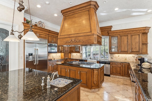 kitchen featuring decorative light fixtures, backsplash, stainless steel appliances, dark stone counters, and an island with sink