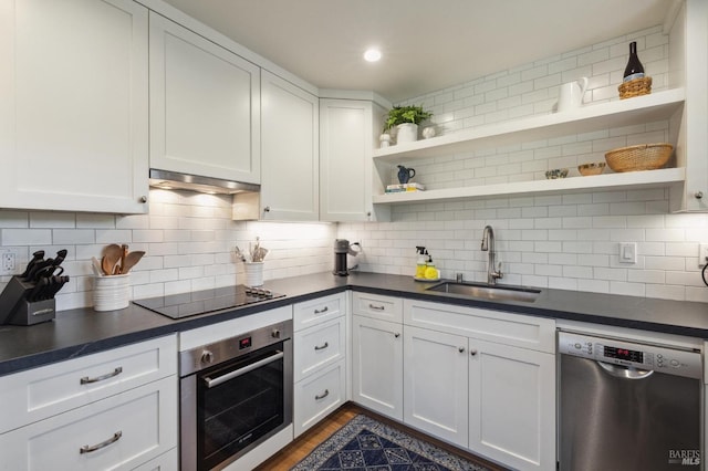 kitchen with sink, tasteful backsplash, range hood, white cabinets, and appliances with stainless steel finishes