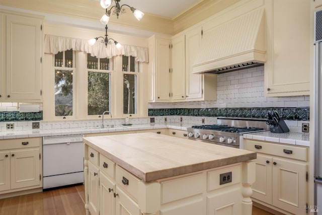 kitchen with stove, custom range hood, white dishwasher, a kitchen island, and butcher block counters