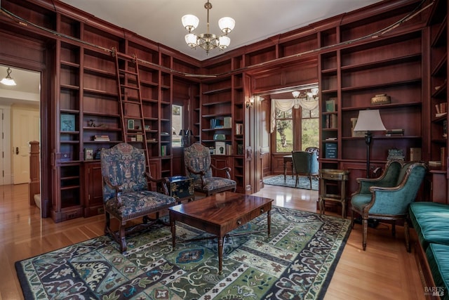 sitting room featuring wood walls, built in features, light hardwood / wood-style floors, and a chandelier