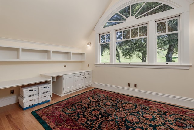 office space with a wealth of natural light, built in desk, lofted ceiling, and light wood-type flooring