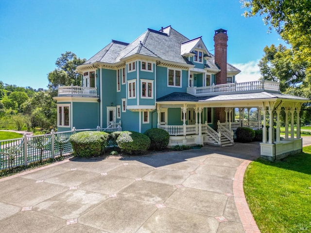 rear view of property featuring a balcony, covered porch, and a yard