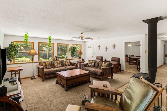 living room with light colored carpet, ceiling fan, a wood stove, and a textured ceiling