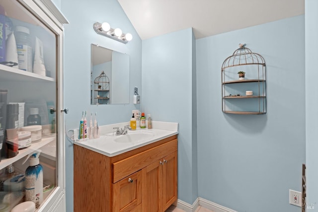 bathroom with baseboards, vanity, and lofted ceiling