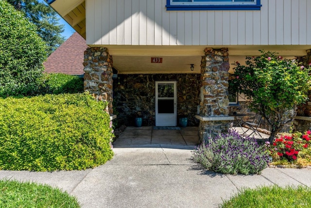 doorway to property with stone siding and roof with shingles