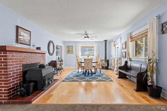 dining room featuring a healthy amount of sunlight, a wood stove, a ceiling fan, and wood finished floors