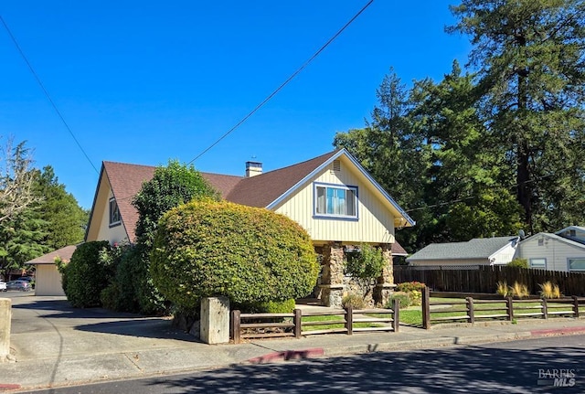 view of front of house with a shingled roof, stone siding, a fenced front yard, and a chimney