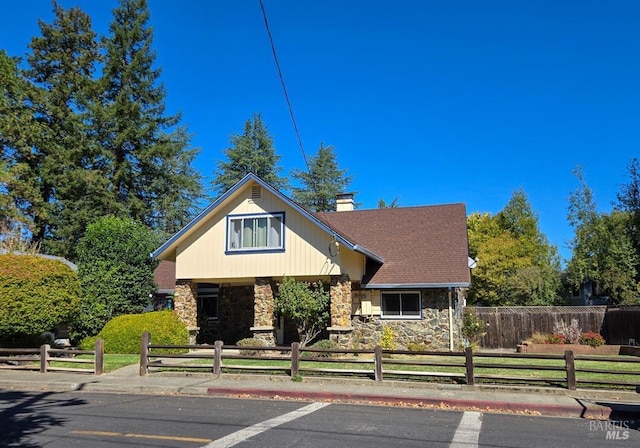 view of front of property with a fenced front yard, stone siding, a chimney, and roof with shingles