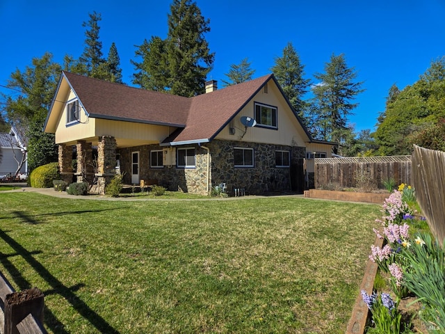 view of front facade with a shingled roof, a front lawn, fence, a chimney, and stone siding