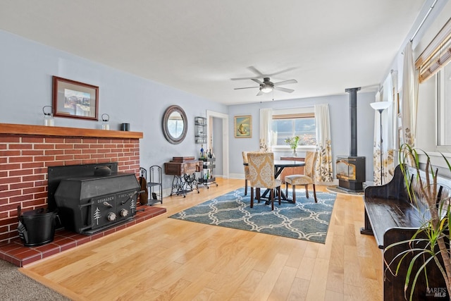 dining space with a wood stove, wood finished floors, and ceiling fan