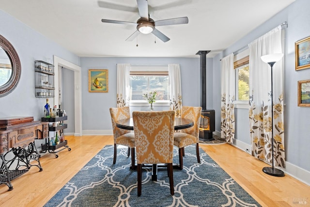 dining area with ceiling fan, baseboards, wood finished floors, and a wood stove