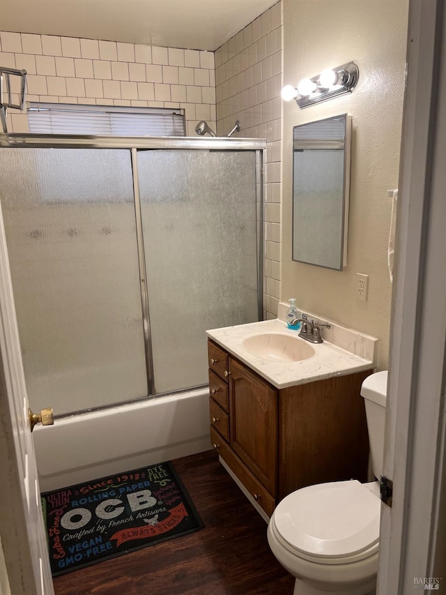 full bathroom with vanity, hardwood / wood-style floors, combined bath / shower with glass door, and toilet