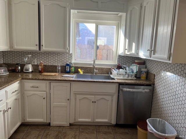 kitchen with sink, white cabinets, backsplash, dark tile patterned flooring, and stainless steel dishwasher