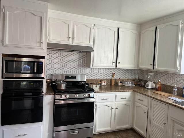 kitchen featuring dark tile patterned floors, appliances with stainless steel finishes, white cabinetry, decorative backsplash, and dark stone counters