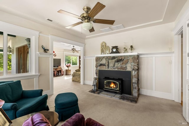 carpeted living room with a raised ceiling, ceiling fan, and a stone fireplace