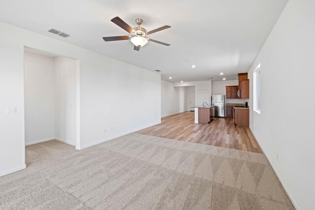 unfurnished living room with light carpet and ceiling fan