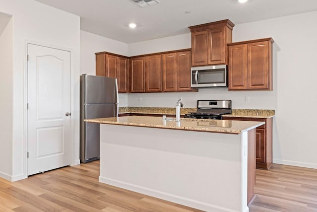 kitchen featuring a kitchen island with sink, light stone counters, light wood-type flooring, and appliances with stainless steel finishes