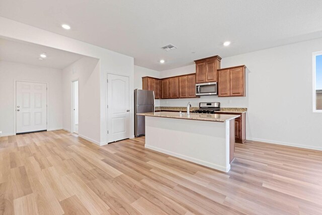 kitchen with sink, light hardwood / wood-style flooring, stainless steel appliances, light stone countertops, and an island with sink