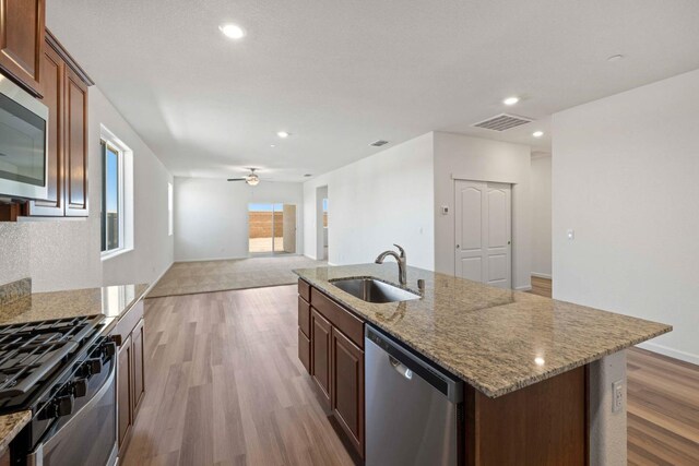 kitchen featuring sink, ceiling fan, stainless steel appliances, light stone countertops, and a center island with sink